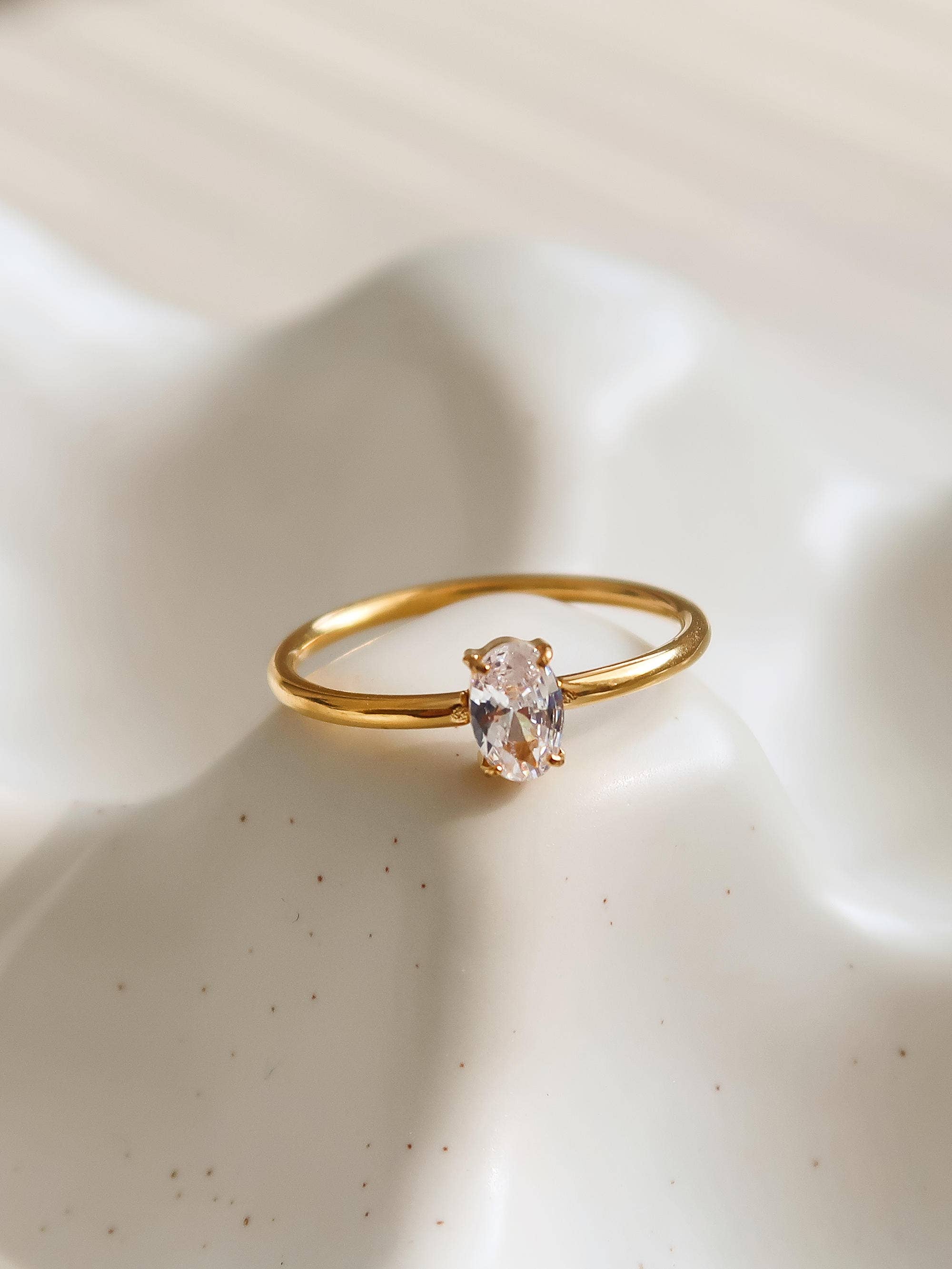 Gold ring with a clear gemstone on a beige surface