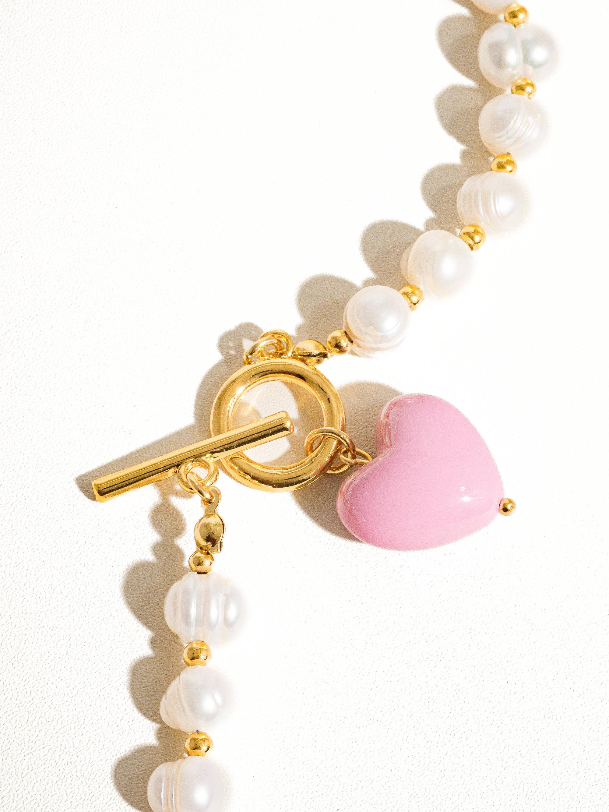 Pearl bracelet with a gold clasp and pink heart charm on a white background