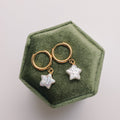Gold earrings with star-shaped pearls on a green hexagonal jewelry box.