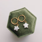 Gold earrings with star-shaped pearls on a green hexagonal jewelry box.