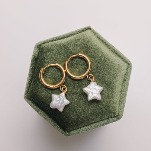 Gold earrings with star-shaped pearls on a green hexagonal jewelry box.