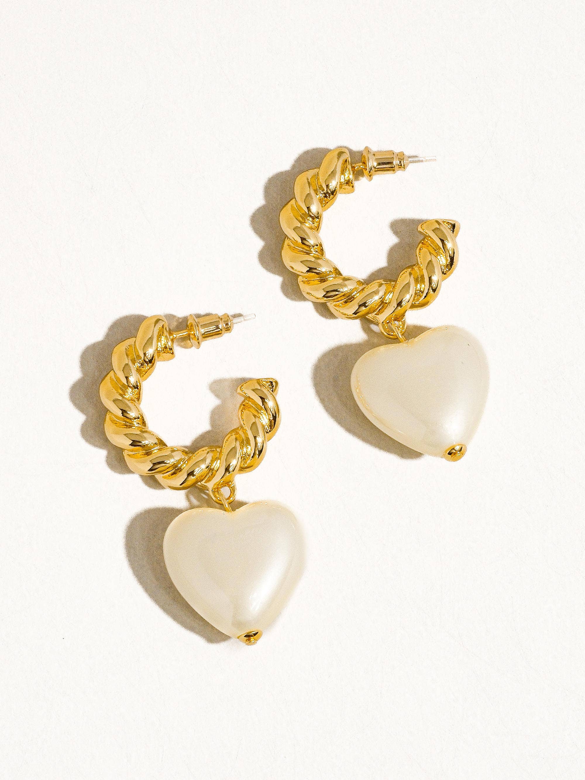 Gold hoop earrings with heart-shaped charms on a white background