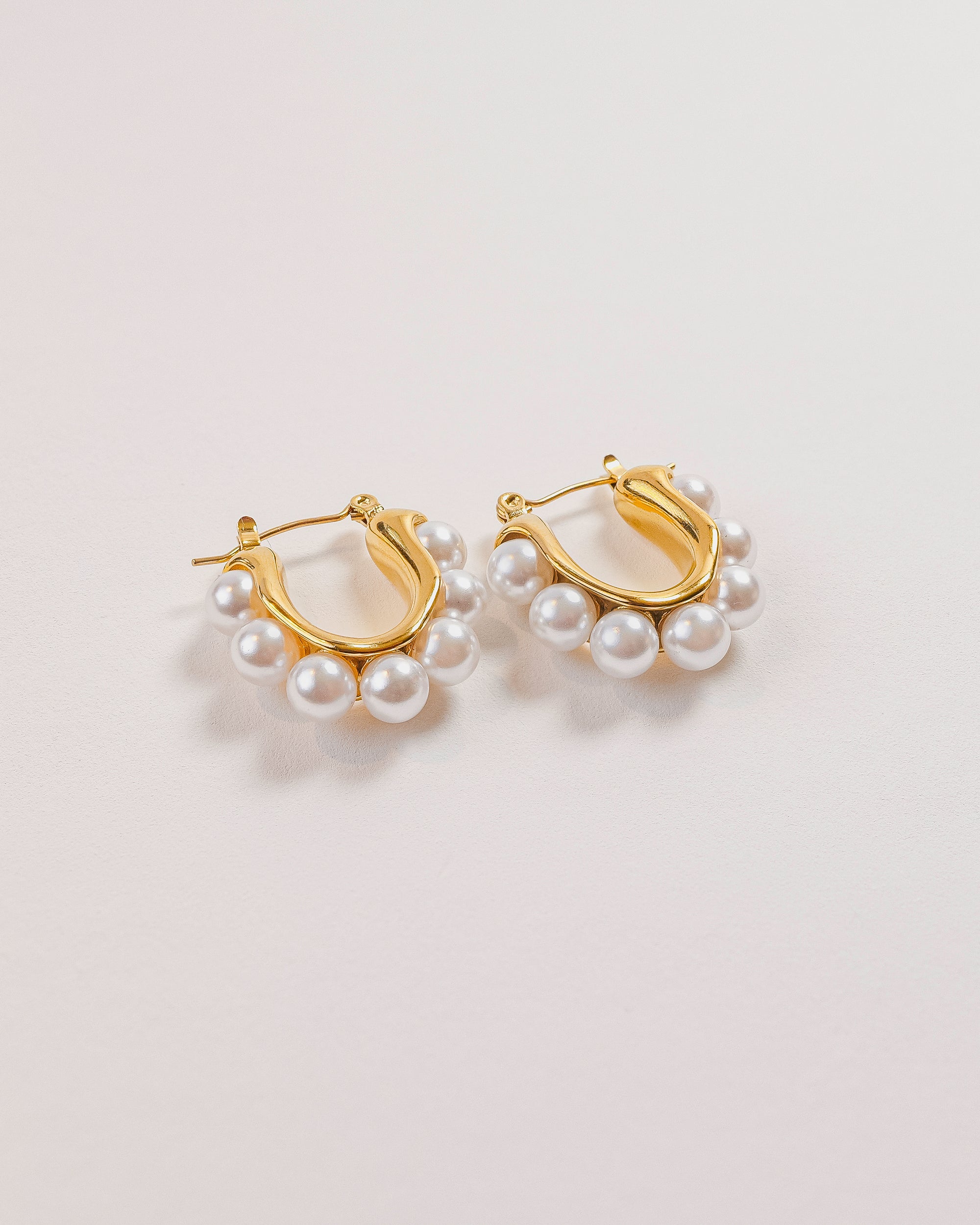 Gold hoop earrings with pearl accents on a light gray background