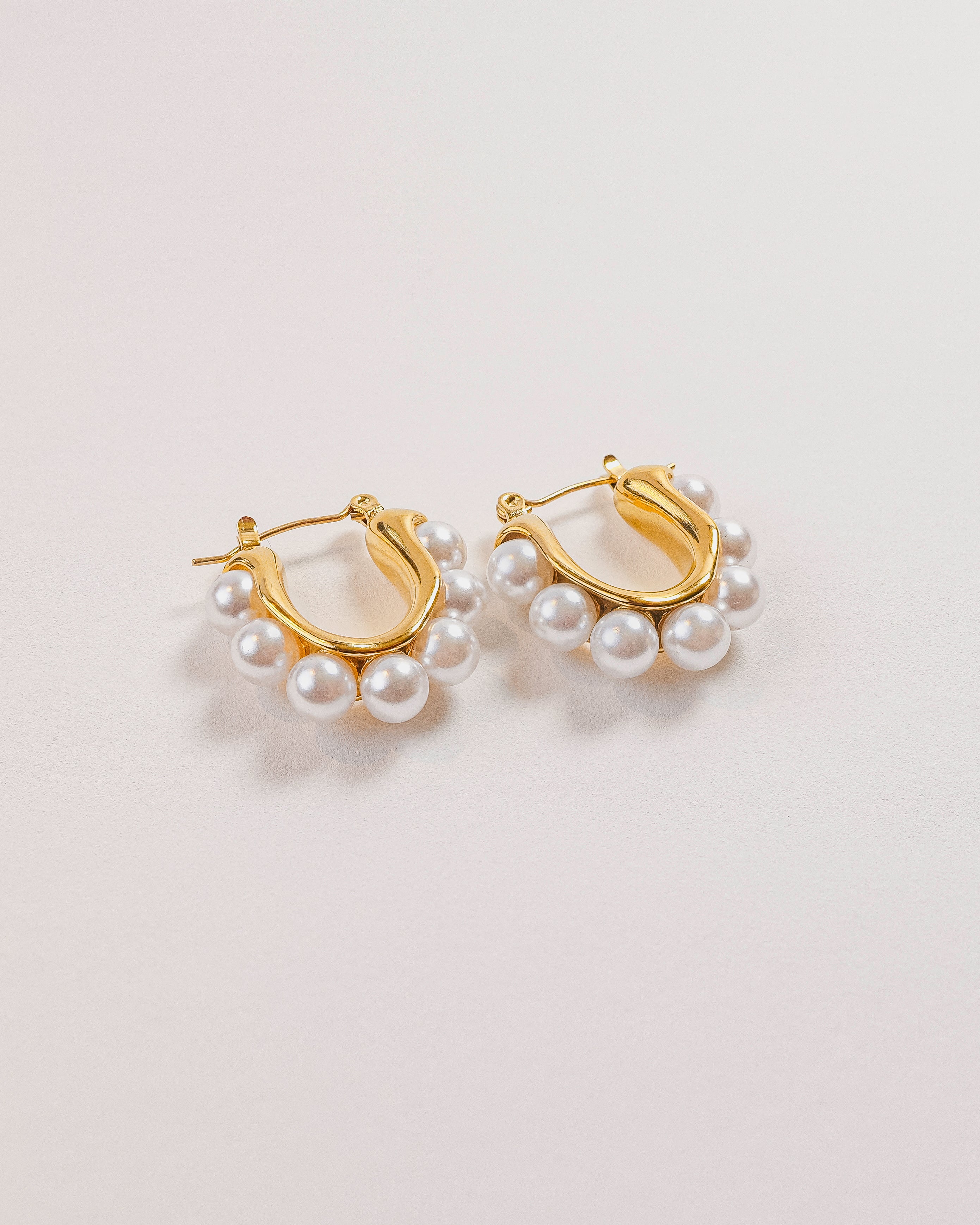 Gold hoop earrings with pearl accents on a light gray background