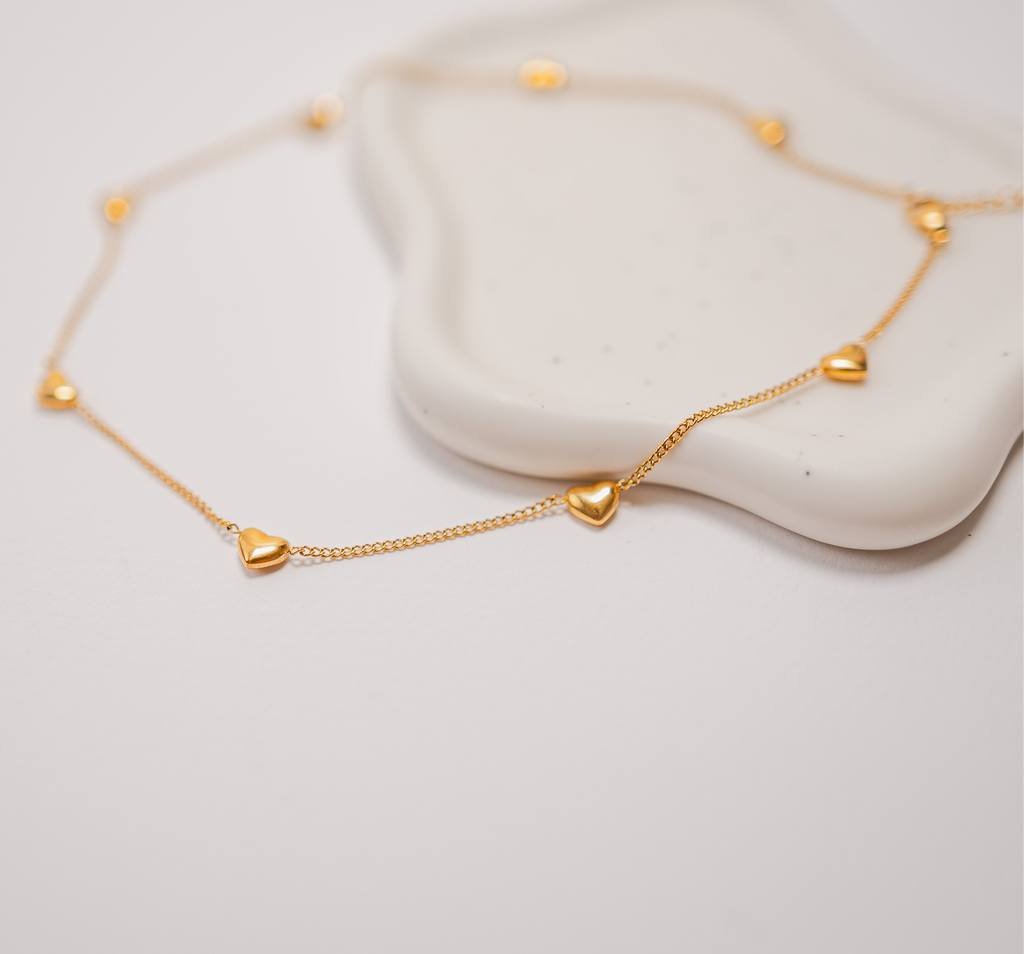 Gold bracelet with heart-shaped charms on a light gray background